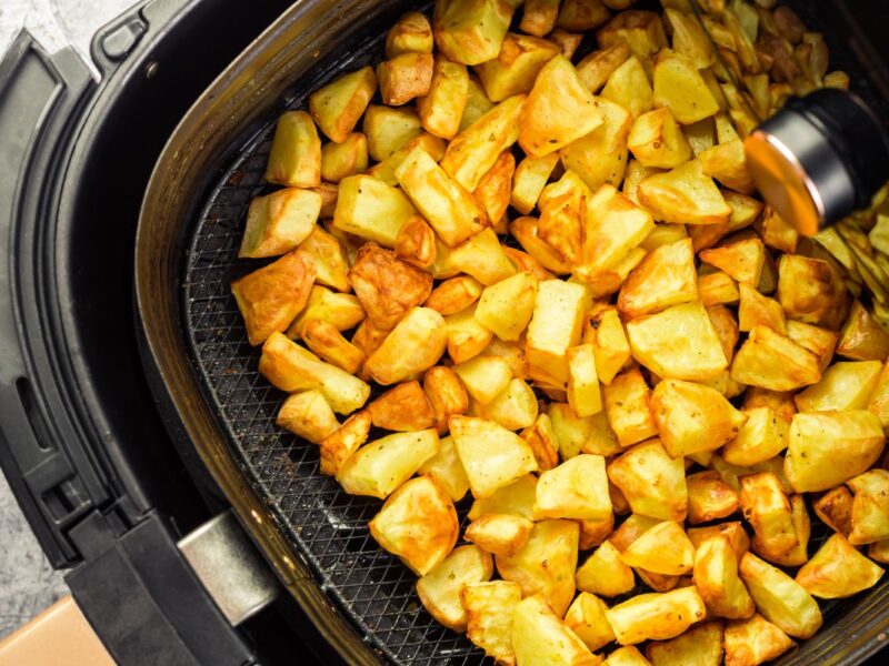 Goldbraune Kartoffelstücke im Korb einer Heißluftfritteuse, appetitlich und knusprig gebacken.