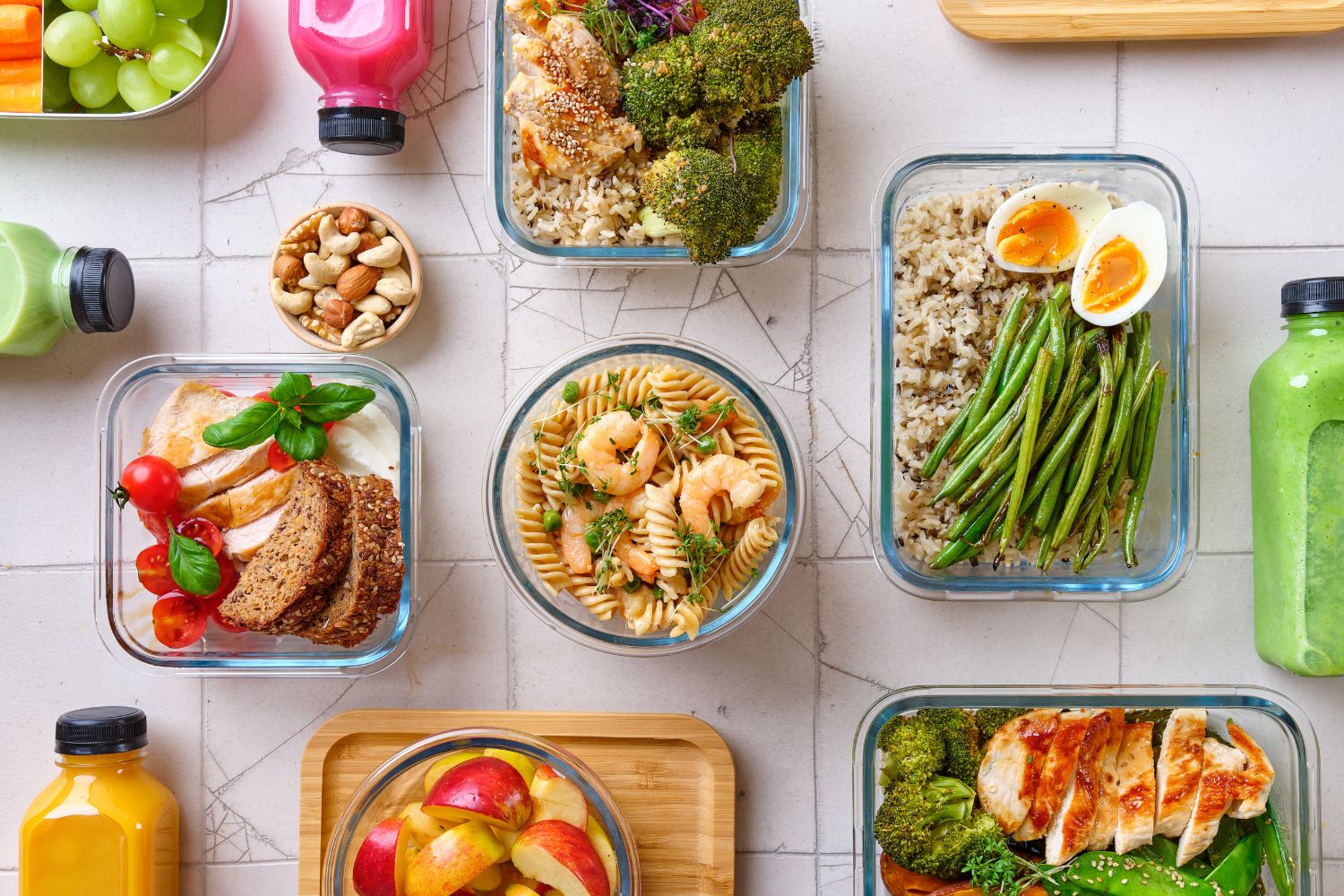 Meal Prep-01 Verschiedene gesunde Gerichte in Glasbehältern, flankiert von bunten Säften und Snacks auf einem Tisch.