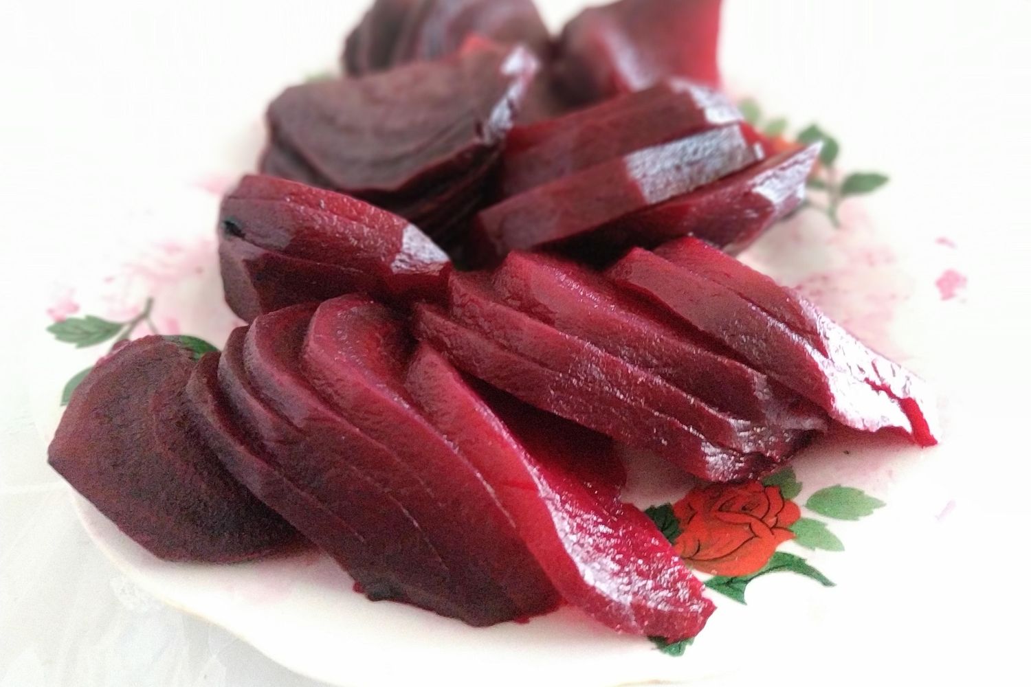 Rote Bete Carpaccio In Scheiben geschnittene Rote Bete auf einem weißen Teller mit Blumenmuster.