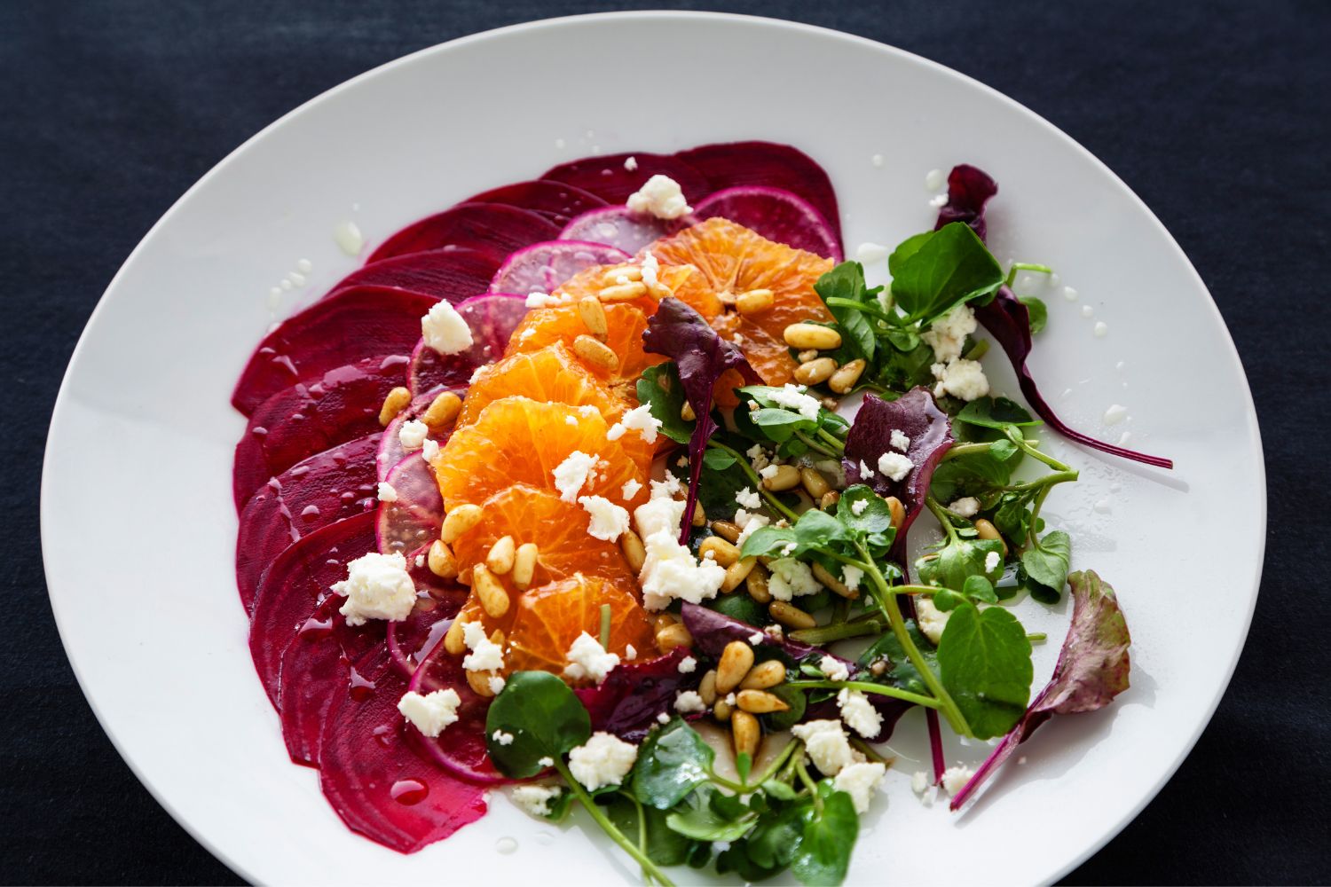 Salatteller mit Rote Bete, Orangen, Ziegenkäse, Pinienkernen und Blattsalat auf einem weißen Teller.