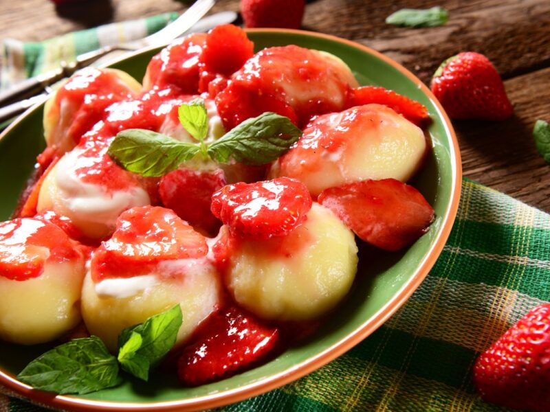 Schüssel mit Erdbeerknödeln, garniert mit frischen Erdbeeren und Minzblättern auf einem Holztisch.