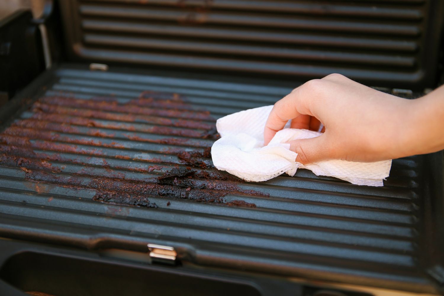 Grillreiniger Hand wischt mit Küchentuch über verschmutzten Grillrost.