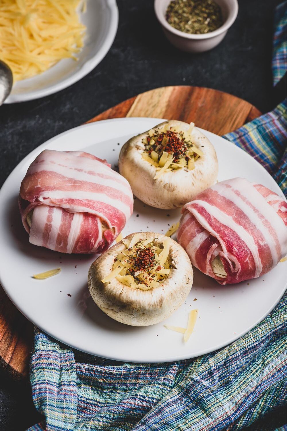 Champignons, gefüllt mit Käse und Gewürzen, teils in Speck gewickelt, auf einem weißen Teller.