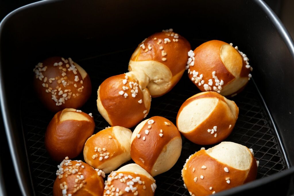 Mehrere goldbraune Laugenbrötchen mit grobem Salz in einem schwarz beschichteten Backblech.