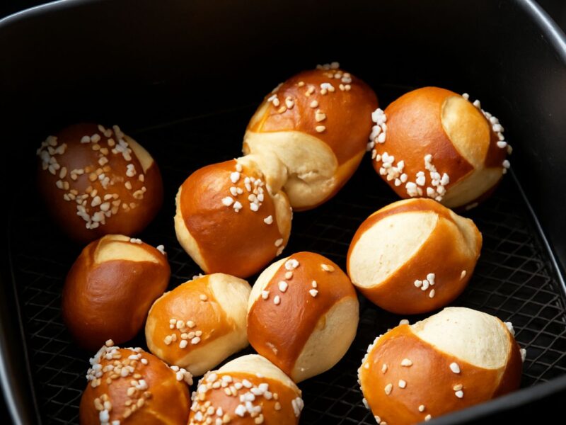 Mehrere goldbraune Laugenbrötchen mit grobem Salz in einem schwarz beschichteten Backblech.