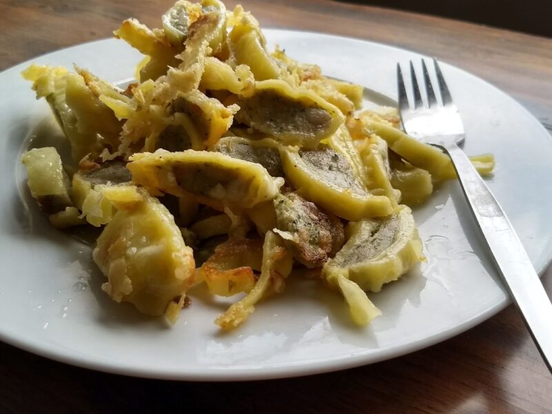 Gebratene Maultaschen auf einem weißen Teller, daneben eine Gabel auf einem Holztisch.