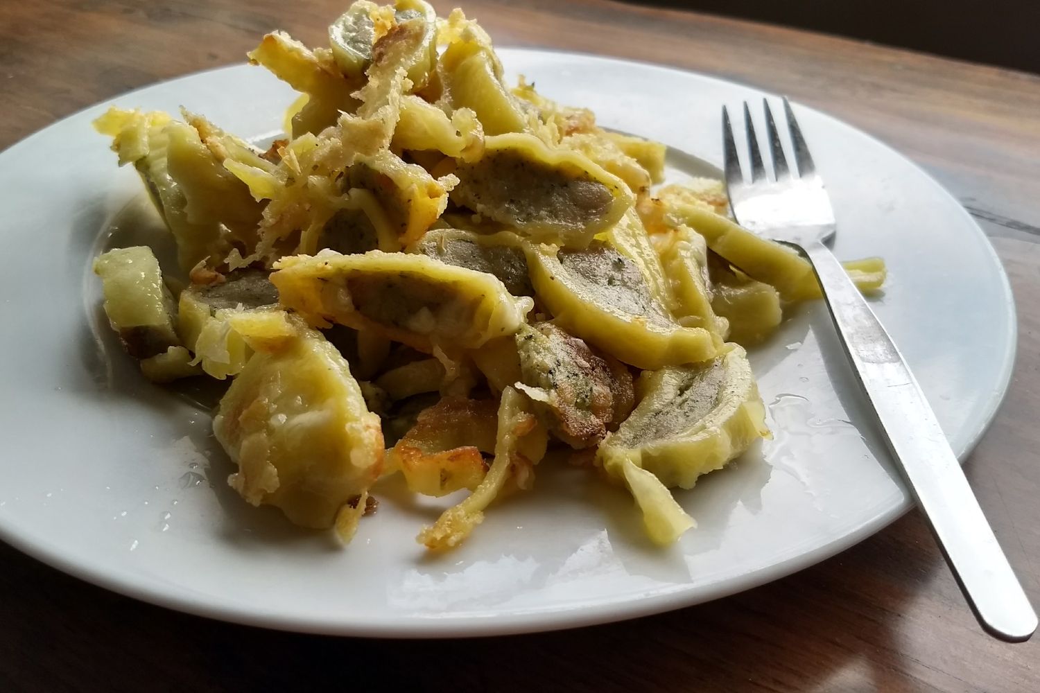 Gebratene Maultaschen auf einem weißen Teller, daneben eine Gabel auf einem Holztisch.