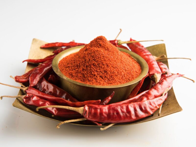 Schale mit rotem Chilipulver, umgeben von getrockneten roten Chilischoten auf einem Teller.
