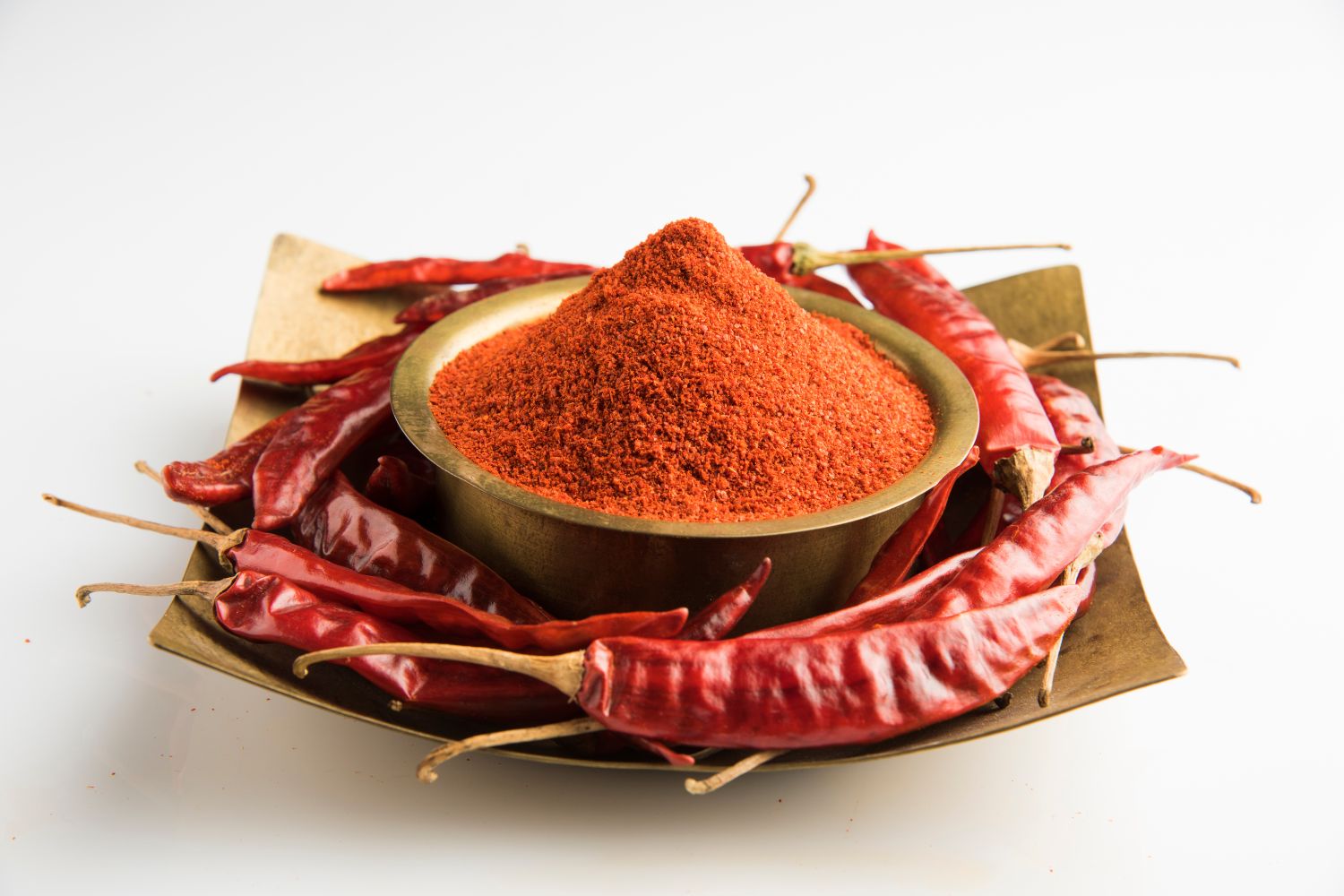Schale mit rotem Chilipulver, umgeben von getrockneten roten Chilischoten auf einem Teller.